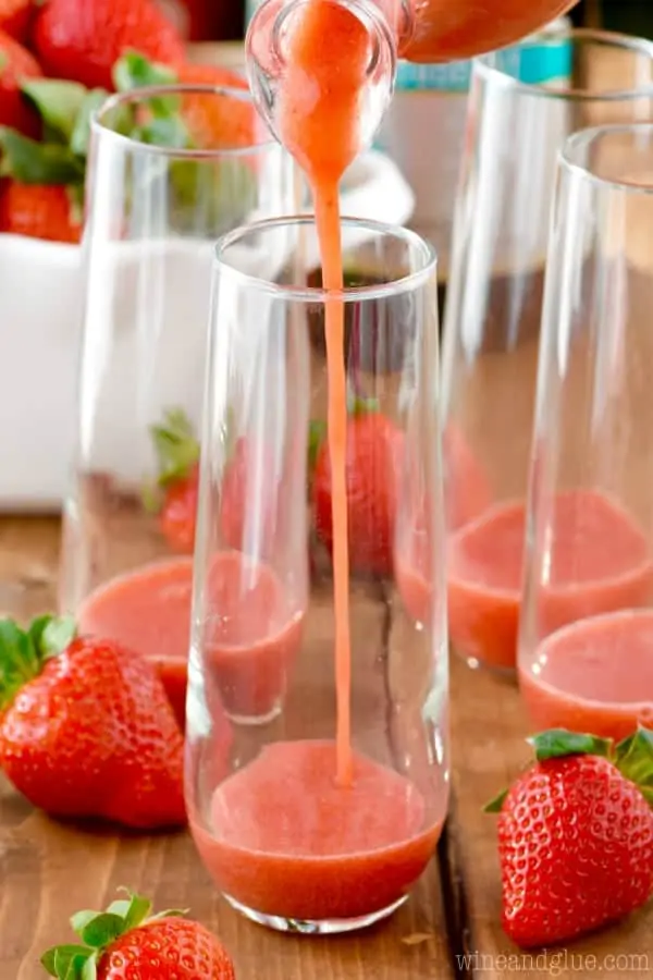 In the champagne glass, the strawberry syrup is being poured for the Strawberry Bellinis. 