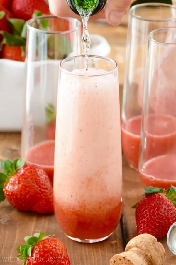 Champagne is being poured into the glass with strawberry syrup inside. 