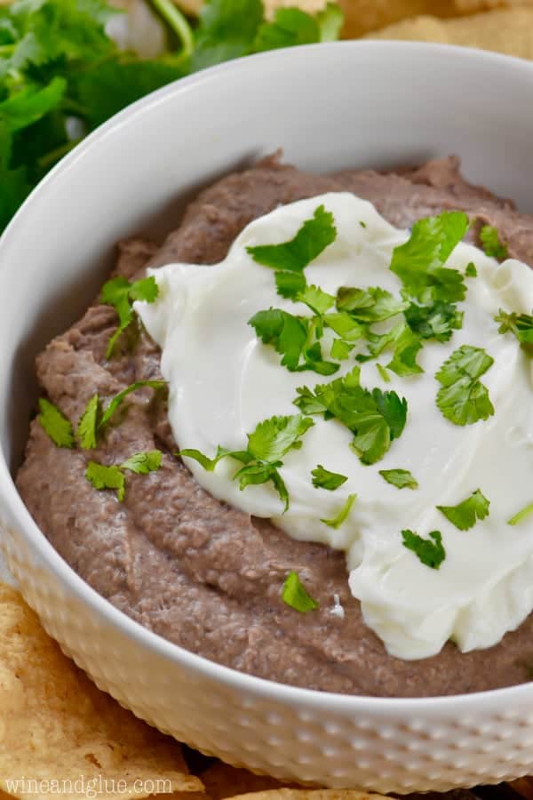 easy black pean dip recipe in a white bowl garnished with sour cream and cilantro