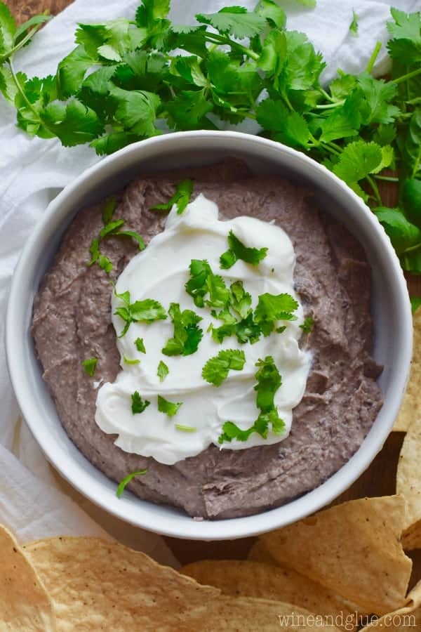 easy black bean dip in a white bowl topped with sour cream and cilantro 