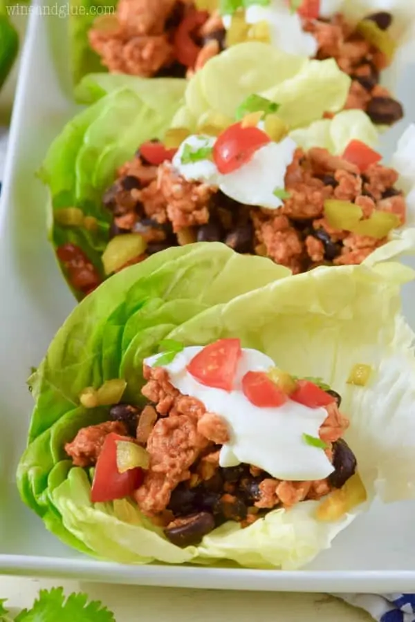 On a white plate, the Five Ingredient Southwestern Lettuce Wraps are filled with black beans, tomatoes, and turkey meat and topped with sour cream and minced jalapenos. 