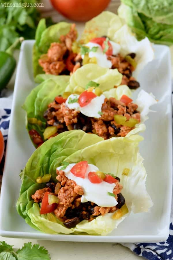 On a white plate, the Five Ingredient Southwestern Lettuce Wraps are filled with black beans, tomatoes, and turkey meat and topped with sour cream and minced jalapenos. 