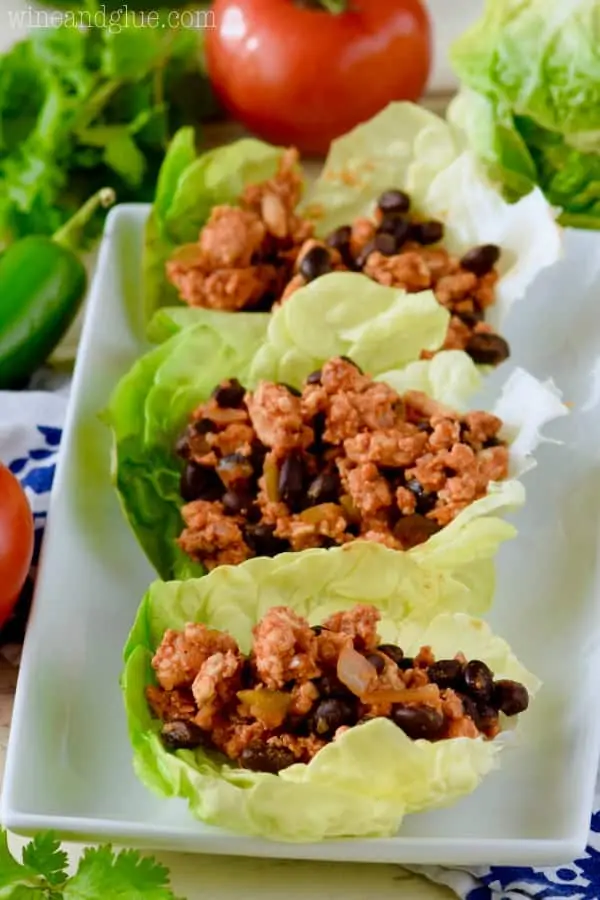 On a white plate, there are three Southwestern Lettuce Wraps filled with a mixture of turkey meat, jalapenos, and black beans. 