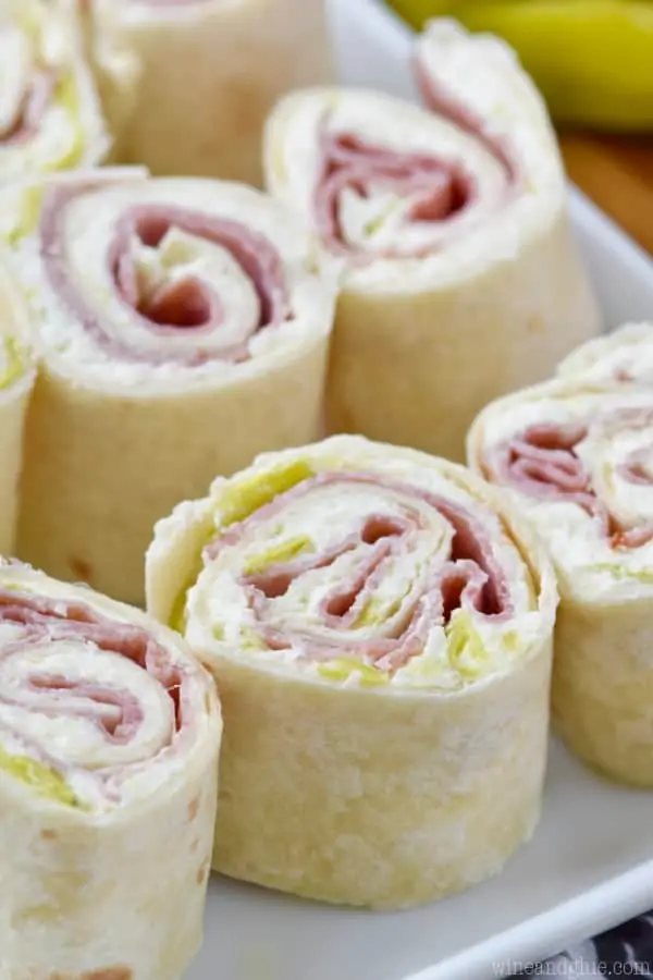 On a white plate, the Italian Pinwheels are in rows. The interior of the Italian Pinwheels show the fillings of pepperoncini, cream cheese, and some deli meat. 