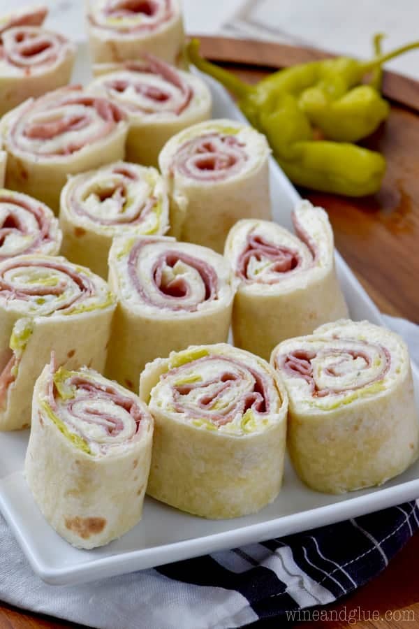On a white plate, the Italian Pinwheels are in rows. The interior of the Italian Pinwheels show the fillings of pepperoncini, cream cheese, and some deli meat. 