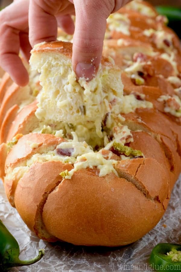 A woman is grabbing a piece of the Jalapeno Popper Pull Apart Bread showing the melted cheese and minced up jalapenos. 