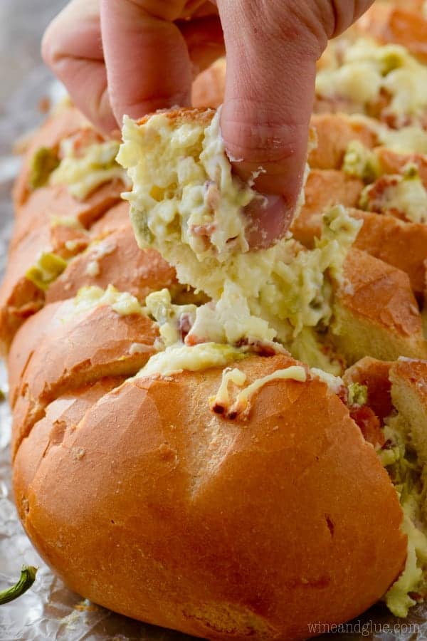 A woman is grabbing a piece of the Jalapeno Popper Pull Apart Bread showing the melted cheese and minced up jalapenos. 