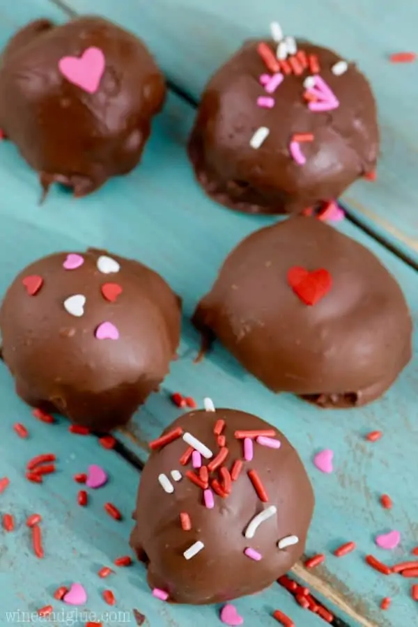 Overhead photo of five Red Velvet Chocolate Ganache Truffles topped with Valentine's day style sprinkles (colors of white, red, and pink; and shapes of hearts and normal sprinkles)