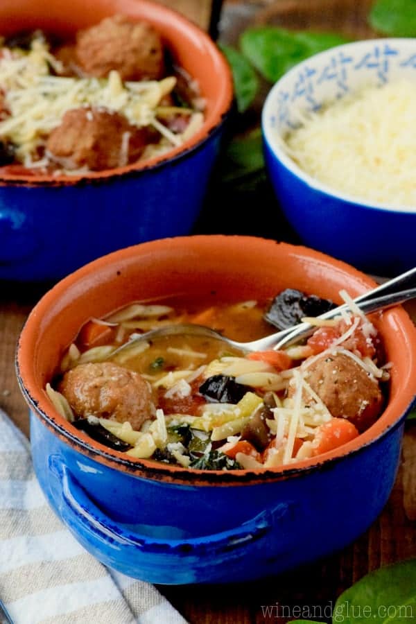 In a blue bowls, the Slow Cooker Vegetable and Meatball Soup is topped with parmesan. 