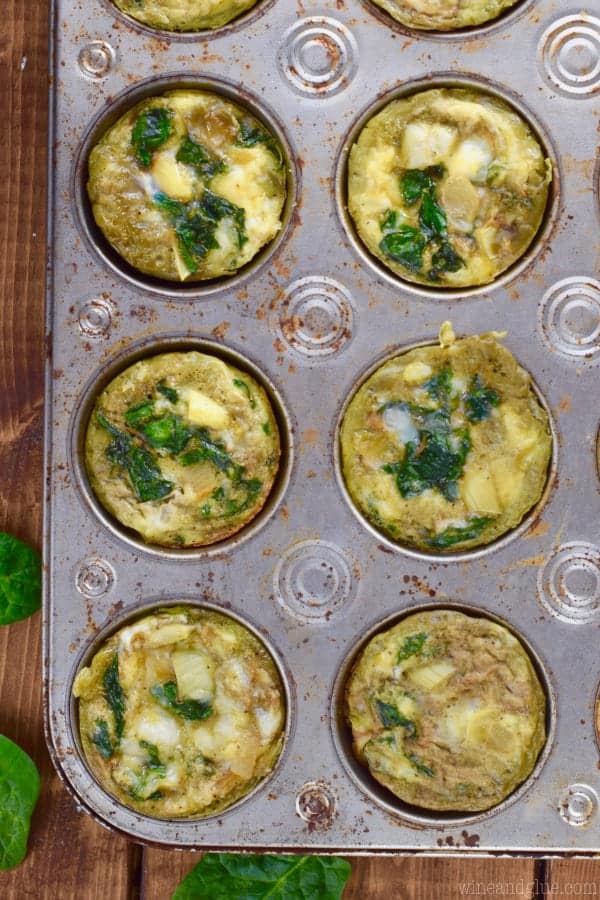 An overhead photo of cooked Spinach and Artichoke Egg Muffins in a muffin tin. 