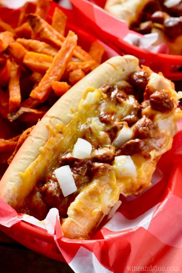 The Oven Baked Chili Cheese Dogs have melted cheese on top with diced white onions, and on the side, are some sweet potato fries. 