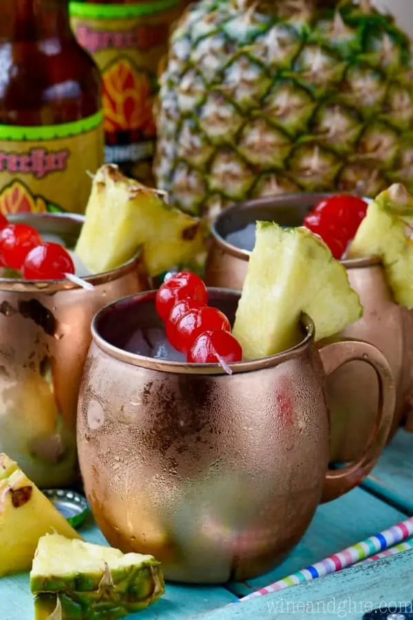 In copper mugs, the Tropical Moscow Mules have ice cubes and on the rim there are sliced pineapples and cherries. 