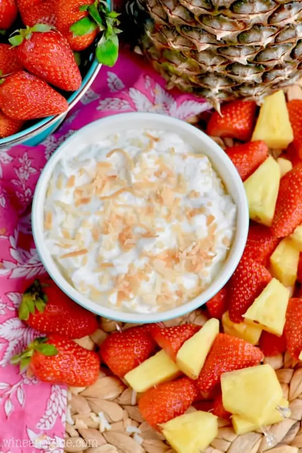 An overhead photo of the Fruit Dip with toasted brown coconut flakes and surrounded by pineapples and strawberries. 