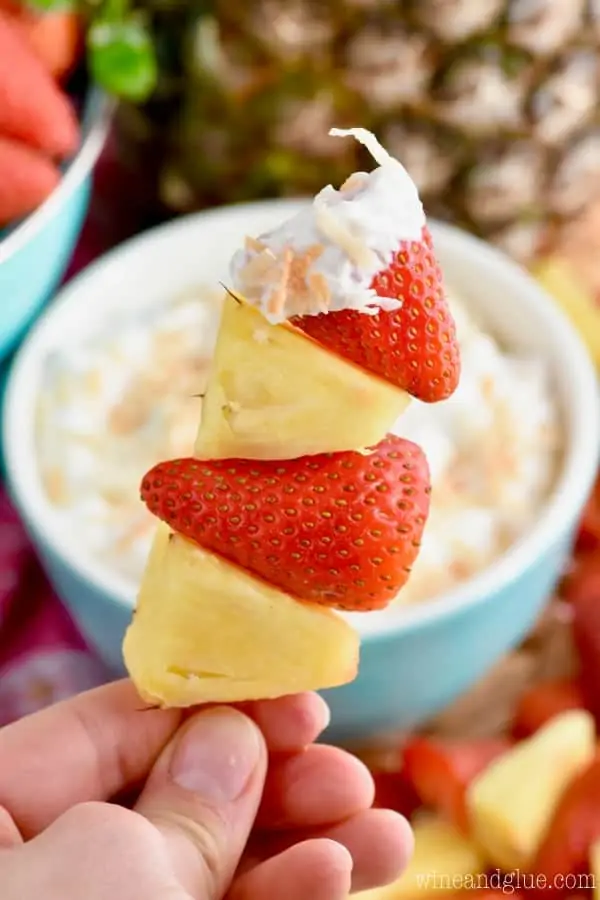 On a toothpick, there are pineapples and strawberries dipped into the Fruit Dip. 