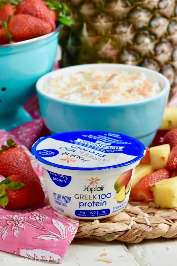 Yoplait's Greek Yogurt that is tropical flavor is in front of the blue bowl filled with the Fruit Dip. 