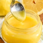 Overhead photo of a spoon dipping into jar of Lemon Curd Recipe. Lemons in the background.