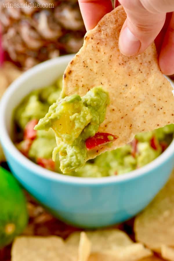 A closeup photo of the Avocado Salsa on the tortilla chip showing the onion and tomato colors on top of the avocado. 