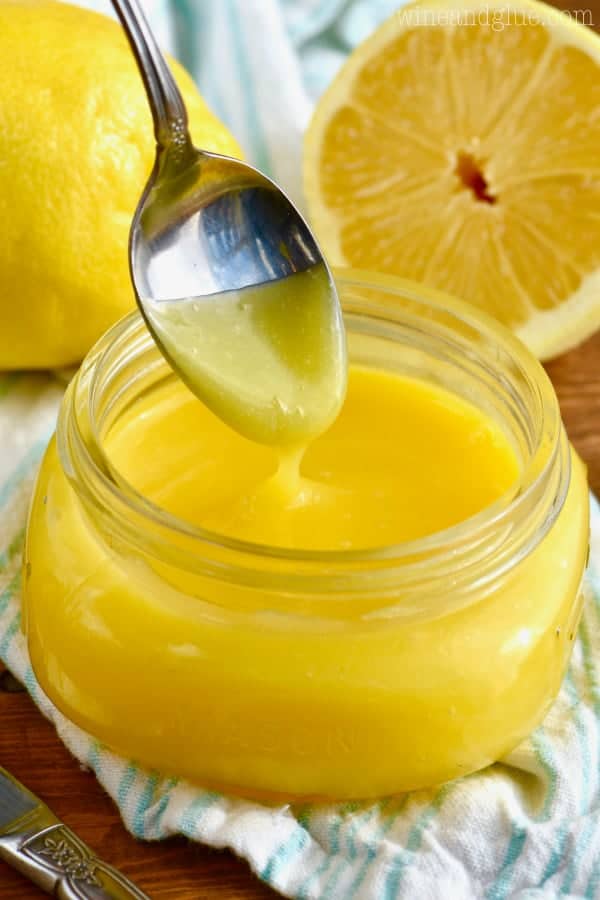 In a small glass bowl, a spoon is being dipped into the glossy Lemon Curd. 