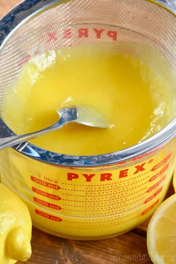 The Lemon Curd is being strained into a large Pyrex measuring cup by a spoon. 