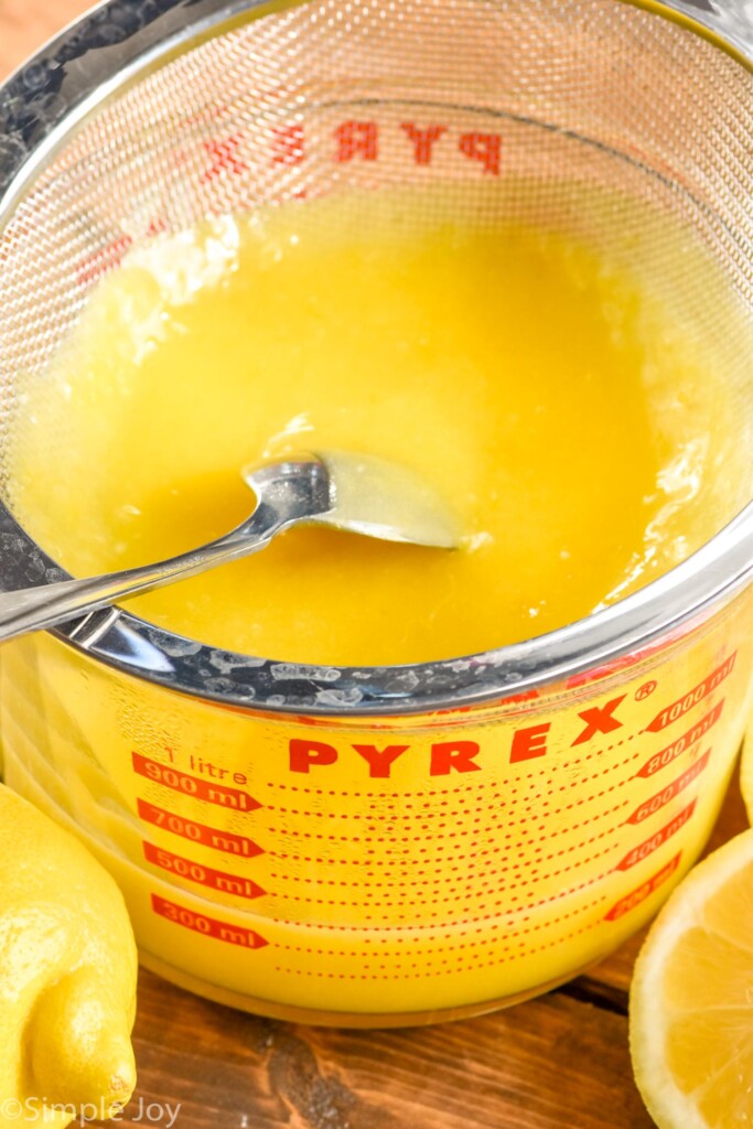 Overhead photo of a glass measuring cup of Lemon Curd Recipe with a spoon for stirring.