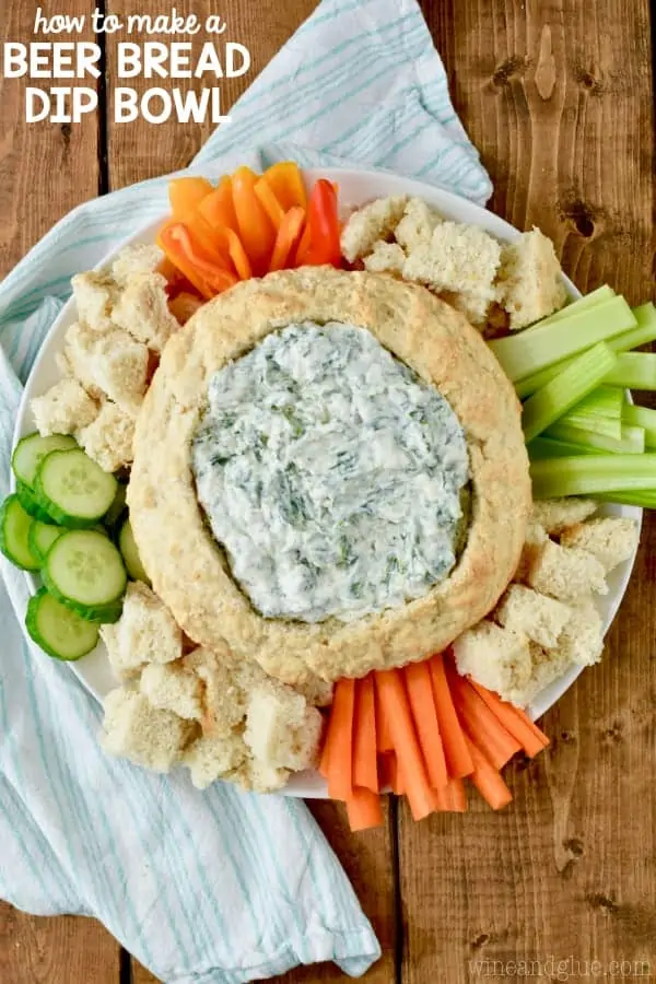 An overhead photo of the Beer Bread Dip Bowl filled with Spinach dip and surrounded with cubed bread, sliced cucumbers, carrots, peppers, and celery. 