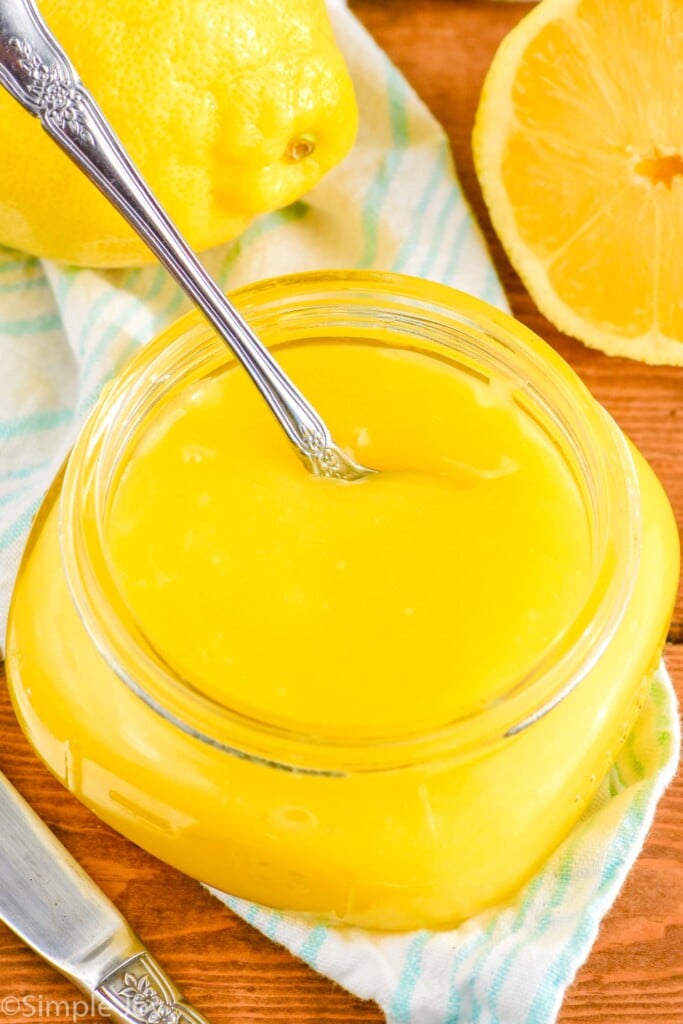 Overhead photo a jar of Lemon Curd Recipe with a spoon for serving. Lemons on counter beside jar.