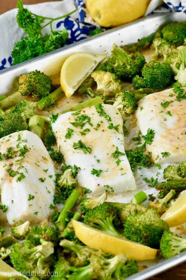 On a sheet pan, three Baked Cods are surrounded by baked asparagus and broccoli