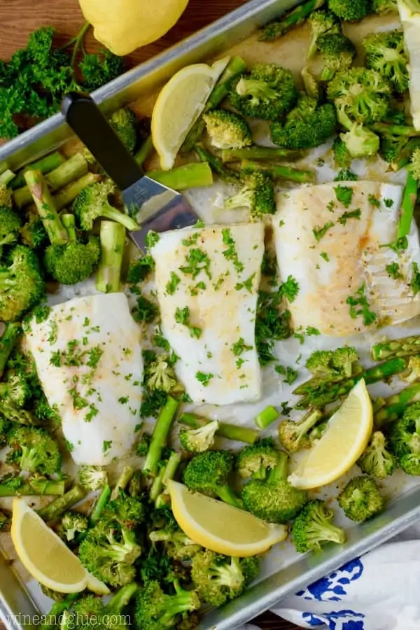 On a sheet pan, three Baked Cods are surrounded by baked asparagus and broccoli