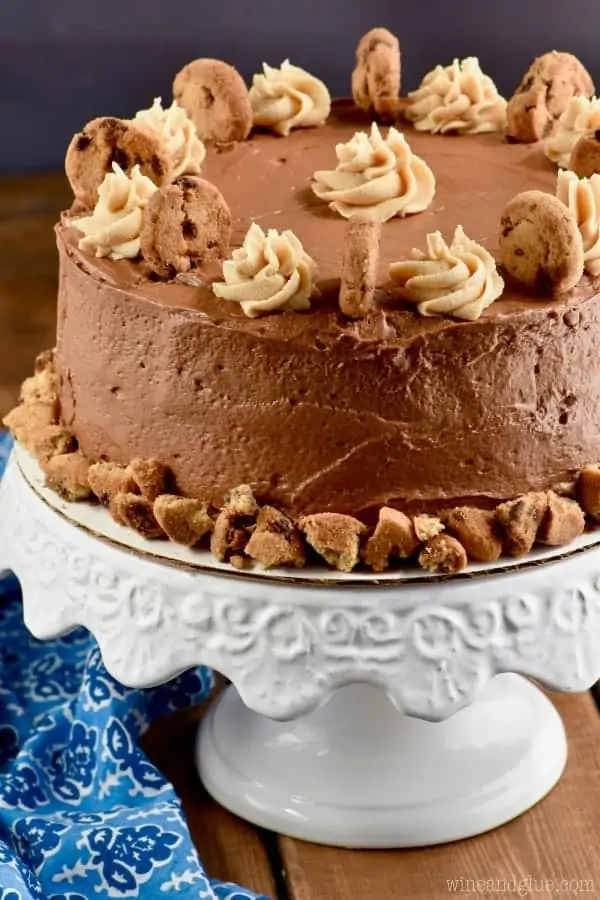 A whole Chocolate Peanut Butter Cookie Cake with a beautiful chocolate frosting. At the bottom of the cake there is crumbled up cookies, and the cake is topped with dollops of peanut butter frosting and cookies. 