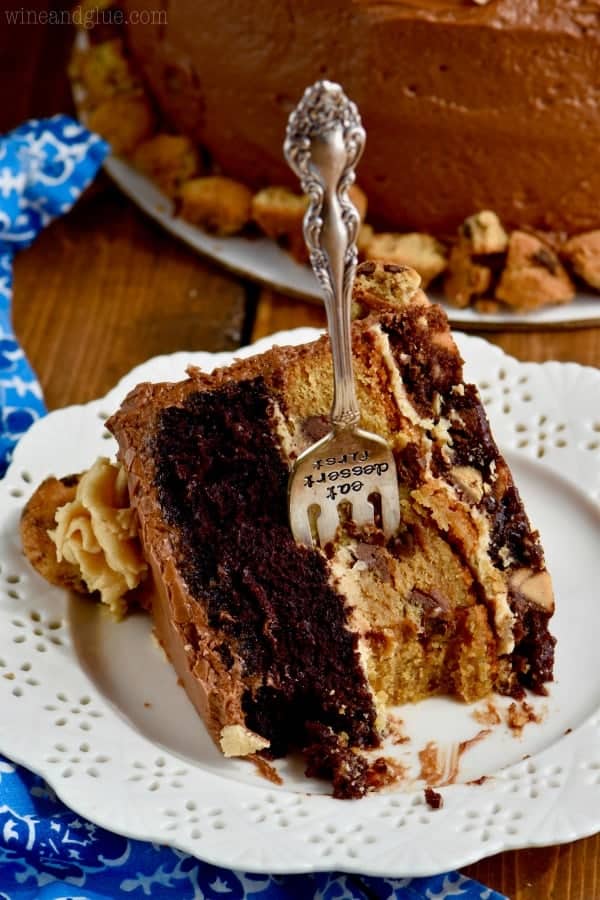 A half eaten slice of the Chocolate Peanut Butter Cookie Cake has three distinct layers of brownie, cookie, and chocolate cake with peanut butter and chocolate frosting. 