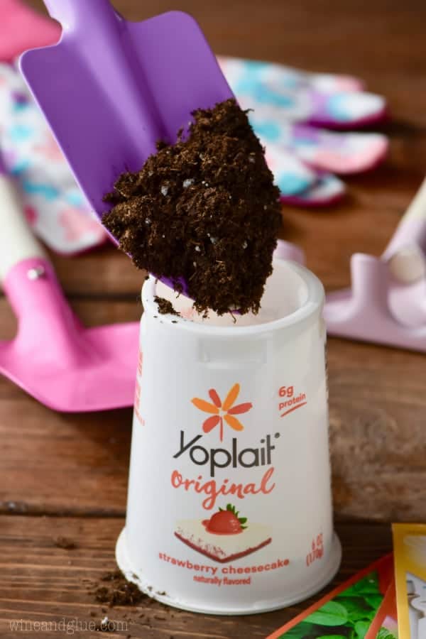 A scoop of soil is being placed into the yogurt cup. 
