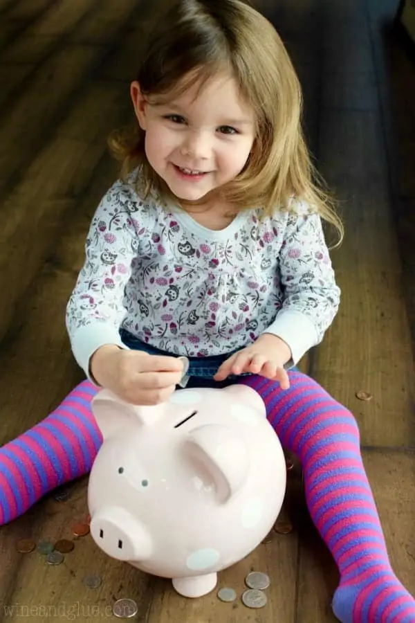 A little girl putting some coins into a pink Piggy Bank