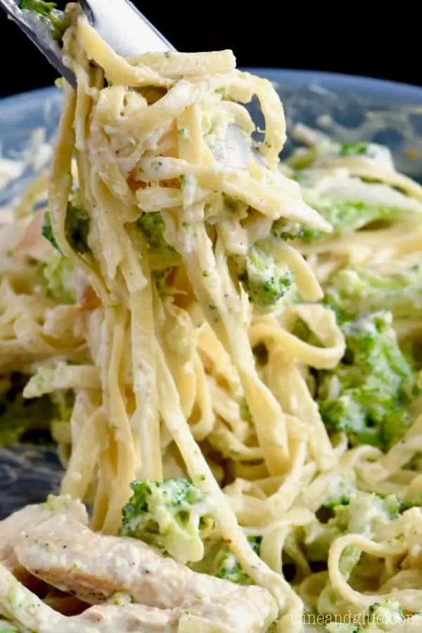 A pair of tongs grabbing a handful of the Lighter Fettuccine Alfredo's pasta, broccoli, and chicken. 