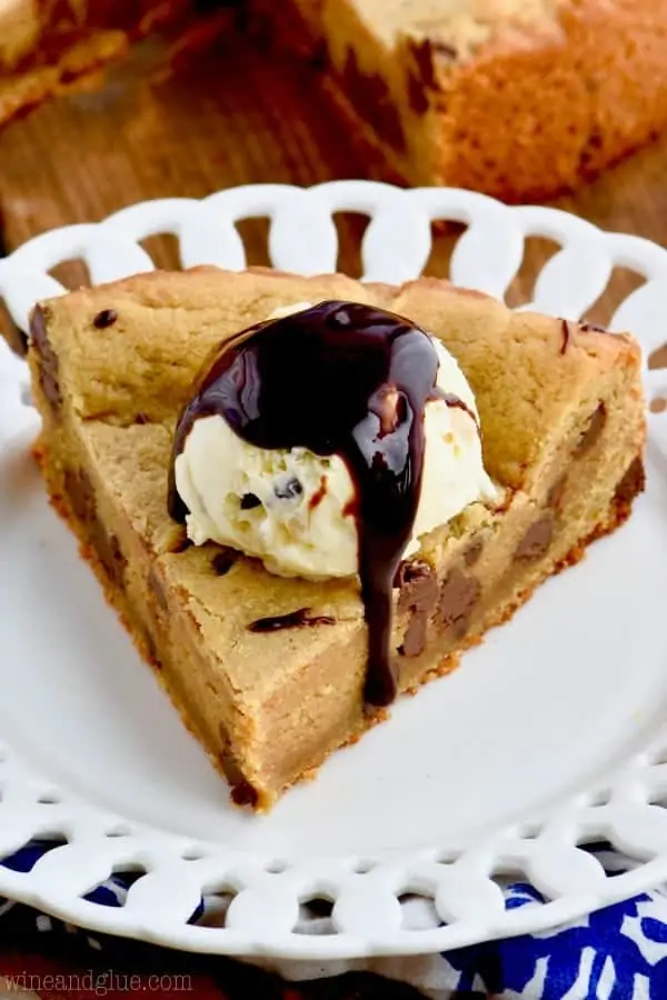 A slice of the Peanut Butter Chocolate Chip Cookie Cake with a scoop of ice cream and drizzled with chocolate syrup