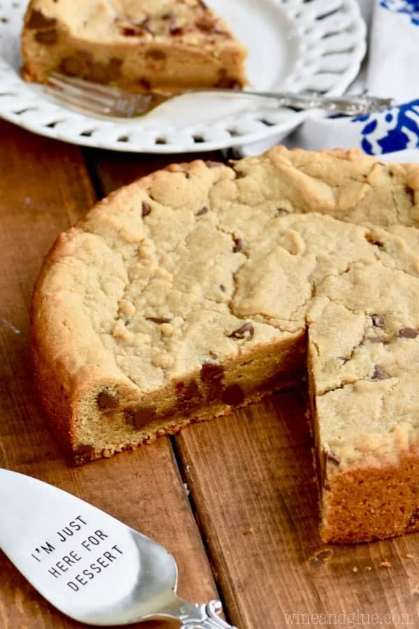 The Peanut Butter Chocolate Chip Cookie Cake has a little slice cut out with a golden brown crust. 