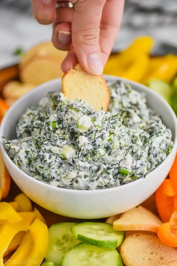 woman dipping a bagel chip into a white bowl full of spinach dip