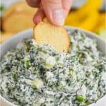 woman dipping a bagel chip into a white bowl full of spinach dip