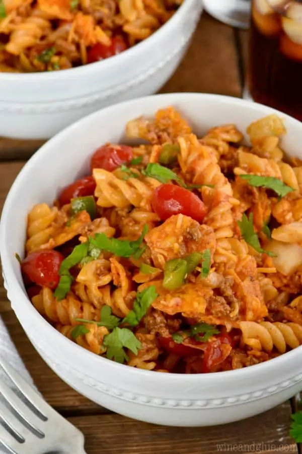 In a small white bowl, the Taco Pasta salad has different shades of red from the halved cherry tomatoes and red sauce. 