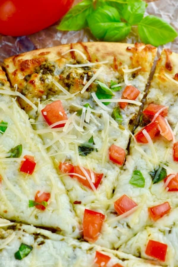 Overhead close up image of pesto pizza garnished with parmesan, basil and tomato