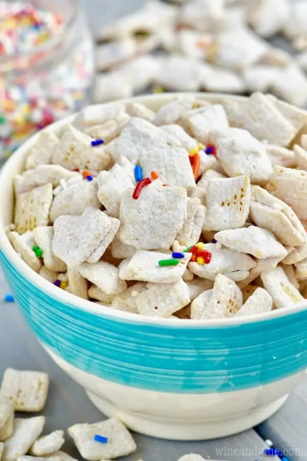 In a blue bowl, the Funfetti Cake Batter Muddy Buddies is powdered with some dry white cake batter and sprinkled with rainbow sprinkles. 