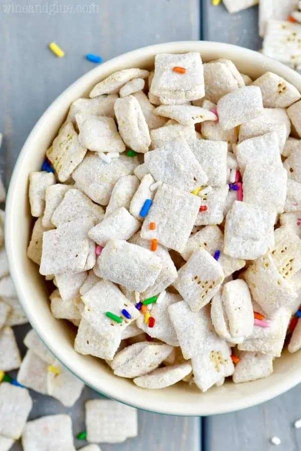 In a blue bowl, the Funfetti Cake Batter Muddy Buddies is powdered with some dry white cake batter and sprinkled with rainbow sprinkles. 