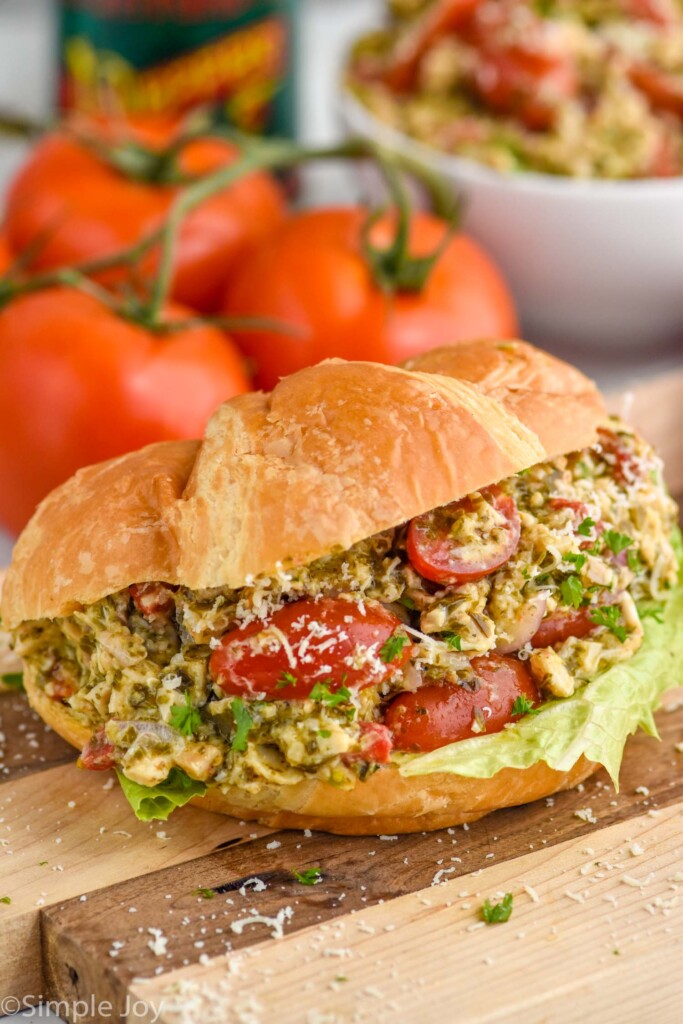 Overhead photo of Pesto Chicken Salad served on a croissant. Tomatoes on counter behind sandwich.