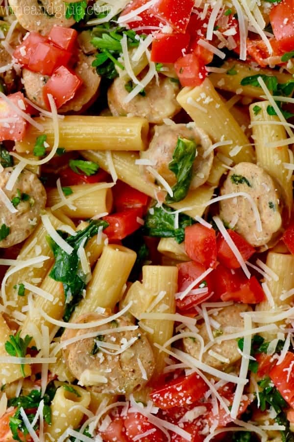 A closeup photo of the Sausage Pasta Skillet showing the diced tomatoes, diced red peppers, sautéed spinach, sliced sausage, and pasta topped with parmesan cheese