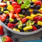pinterst graphic of fruit salad in a bowl that is topped with a mint leaf sprig