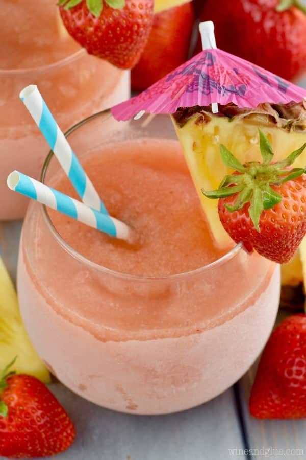 An overhead photo of the Frozen Sangria Slush with two paper straws in it and sliced pineapples and strawberries on the rim. 