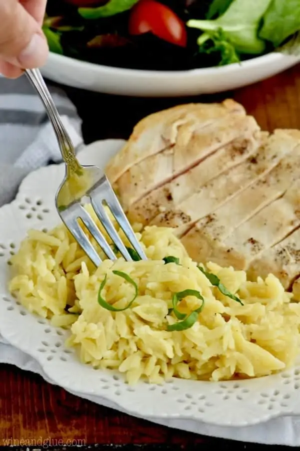 On a white plate, the Cheesy Orzo is paired with some chicken breast and a simple salad. 