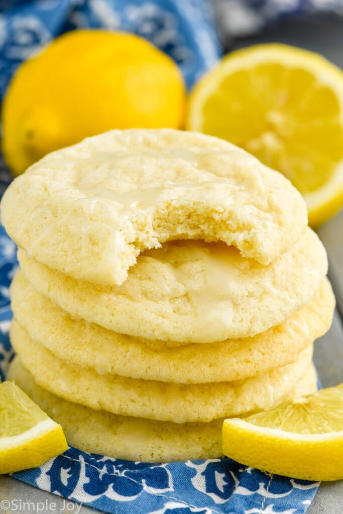 Close up photo of a stack of Lemon Sugar Cookies surrounded by lemons. Bite taken out of top cookie.