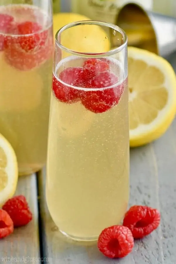 In a champagne fluke, the Lemon Champagne Cocktail has a yellow tint and topped with raspberries