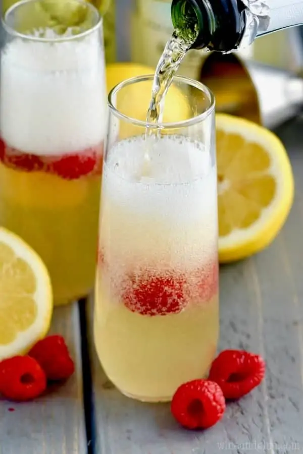 Champagne is being poured into the Lemon Champagne Cocktail which has raspberries