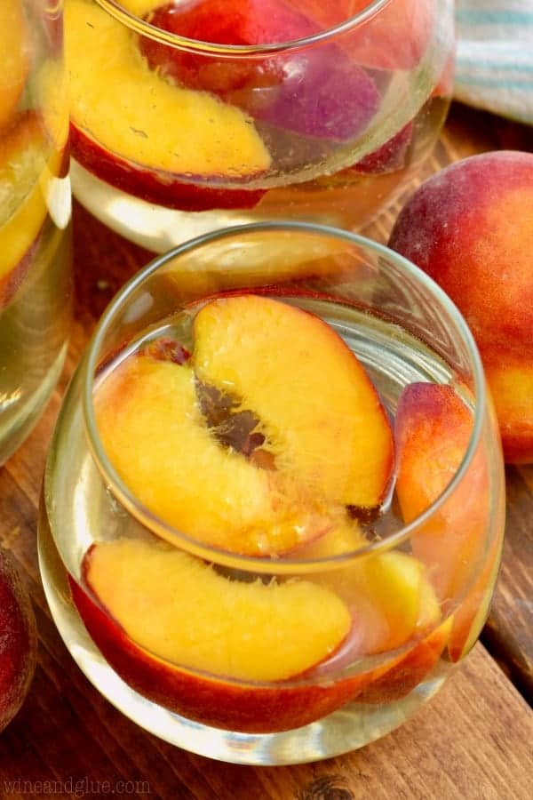glass of peach sangria with fresh peaches in it